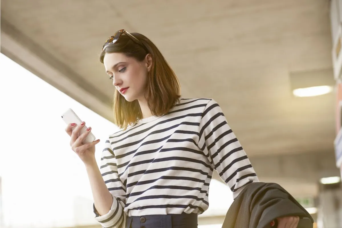 Woman commuter with mobile and suitcase waiting